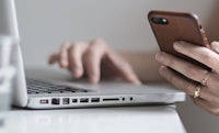 a woman's hand holding a phone next to a laptop